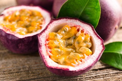Photo of Fresh passion fruits and green leaves on wooden table, closeup