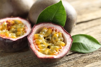 Photo of Fresh passion fruits and green leaves on wooden table, closeup