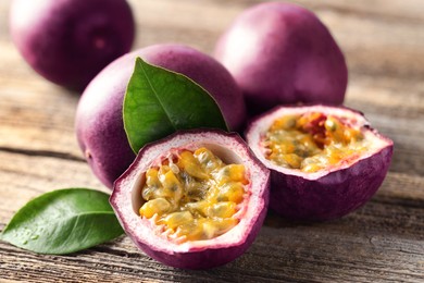 Photo of Fresh passion fruits and green leaves on wooden table, closeup