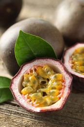 Photo of Fresh passion fruits and green leaves on wooden table, closeup