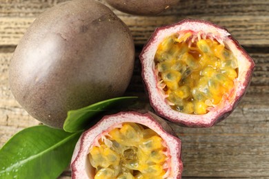 Photo of Fresh passion fruits and green leaves on wooden table, flat lay