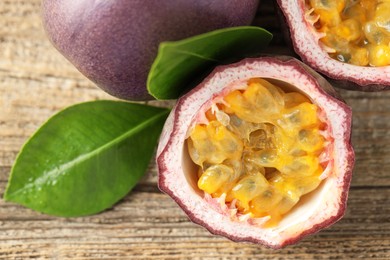 Photo of Fresh passion fruits and green leaves on wooden table, flat lay