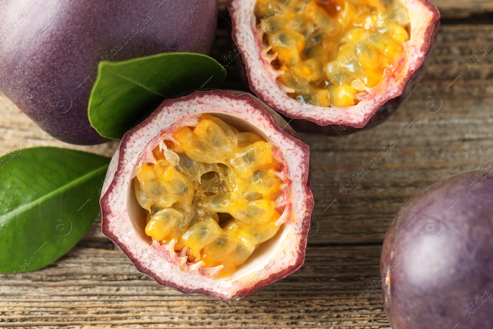 Fresh passion fruits and green leaves on wooden table, flat lay Photo of Fresh passion fruits and green leaves on wooden table, flat lay