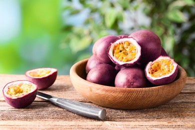 Photo of Fresh passion fruits in bowl and knife on wooden table outdoors, closeup