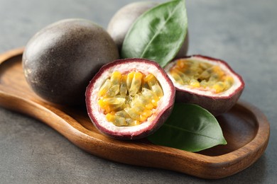 Photo of Fresh passion fruits and green leaves on grey table, closeup