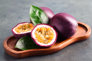 Photo of Fresh passion fruits and green leaves on grey table, closeup