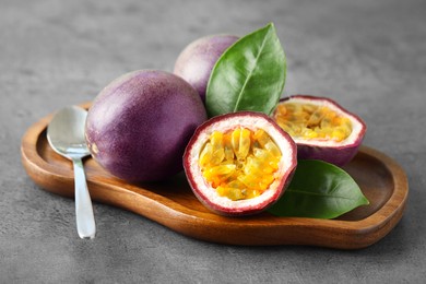 Photo of Fresh passion fruits and green leaves on grey table, closeup