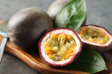 Photo of Fresh passion fruits and green leaves on grey table, closeup