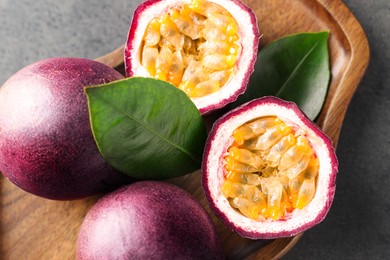 Photo of Fresh passion fruits and green leaves on grey table, top view