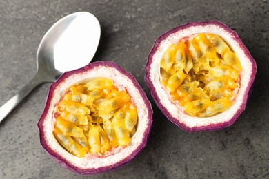 Photo of Halves of fresh passion fruit and spoon on grey table, flat lay