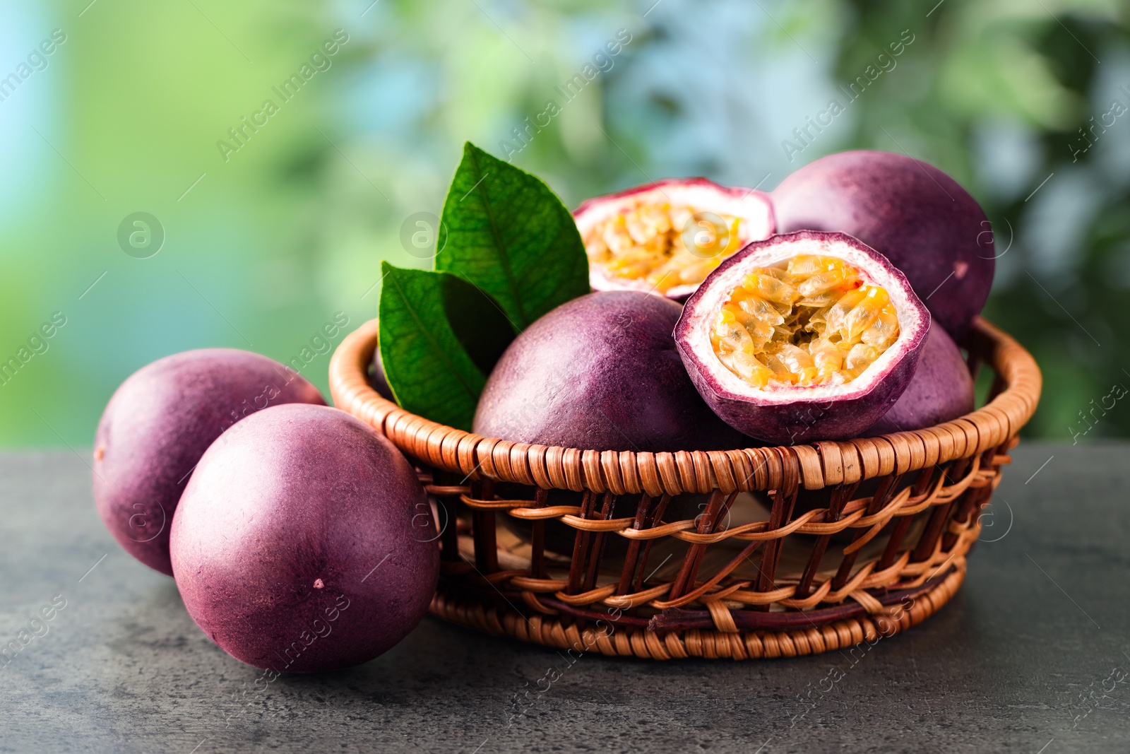 Photo of Fresh passion fruits in wicker basket on grey table outdoors, closeup