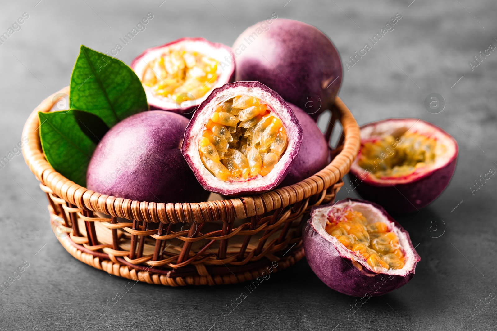 Photo of Fresh passion fruits in wicker basket on grey table, closeup
