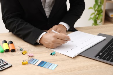 Photo of Man using business planner at wooden table in office, closeup