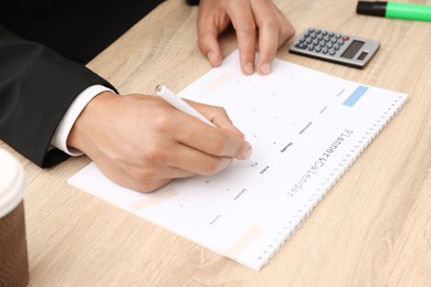 Photo of Man using business planner at wooden table in office, closeup