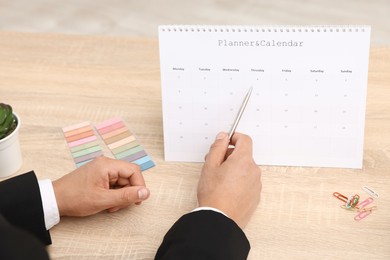 Photo of Man using business planner at wooden table in office, closeup
