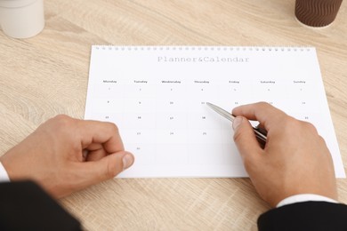 Photo of Man using business planner at wooden table in office, closeup
