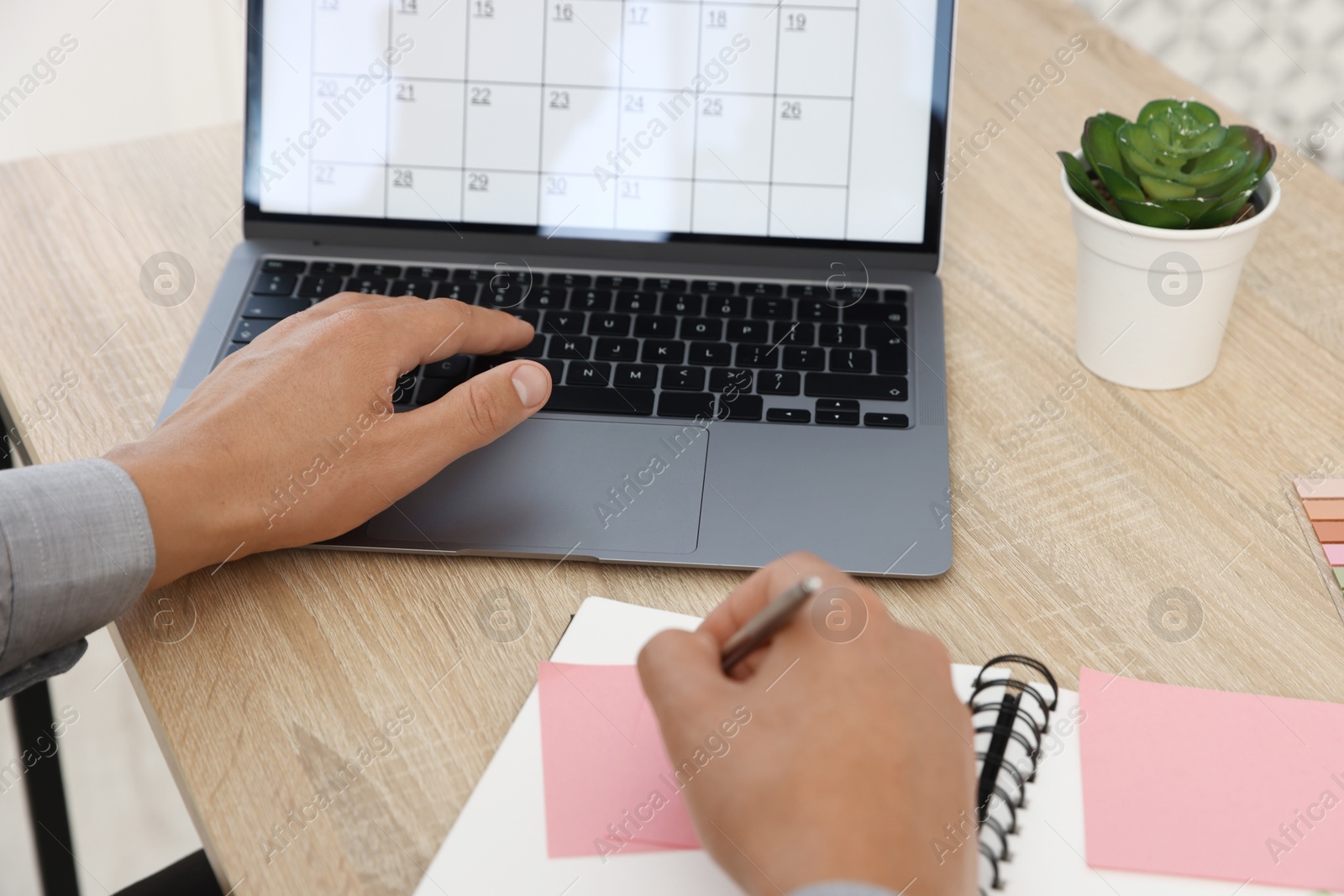 Man writing in business planner and using laptop at wooden table in office, closeup Photo of Man writing in business planner and using laptop at wooden table in office, closeup