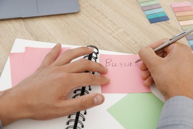 Photo of Man writing in business planner at wooden table in office, closeup