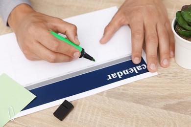 Photo of Business planning. Man using calendar at wooden table in office, closeup