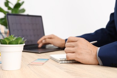 Photo of Man using business planner and laptop at wooden table in office, closeup