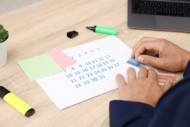 Photo of Business planning. Man with calendar at wooden table in office, closeup