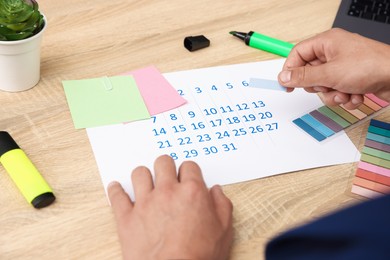 Photo of Business planning. Man with calendar at wooden table in office, closeup