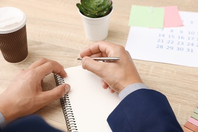 Photo of Man using business planner at wooden table in office, closeup