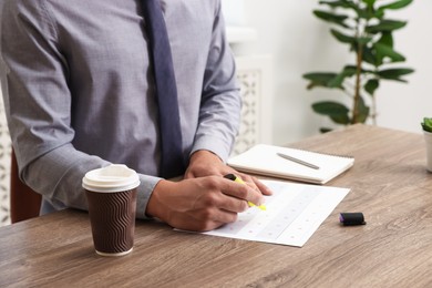 Photo of Man writing in business planner at wooden table in office, closeup