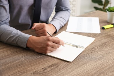 Photo of Man writing in business planner at wooden table in office, closeup