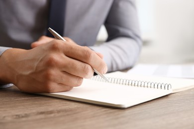 Photo of Man writing in business planner at wooden table in office, closeup