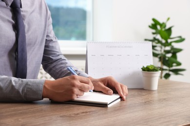 Photo of Man writing in business planner at wooden table in office, closeup