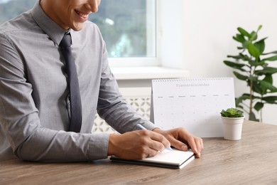 Photo of Man writing in business planner at wooden table in office, closeup