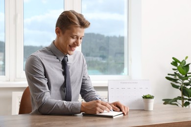 Photo of Man using business planner at wooden table in office