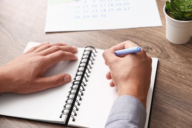 Photo of Man writing in business planner at wooden table in office, closeup