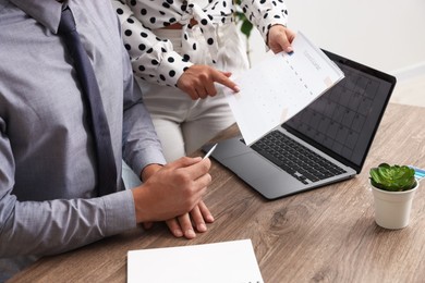 Photo of Woman and man using business planner at wooden table in office, closeup