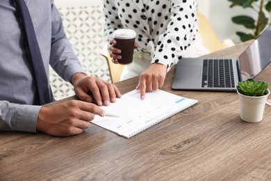 Photo of Woman and man using business planner at wooden table in office, closeup