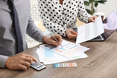 Photo of Business planning. Woman and man with calendar and documents at wooden table in office, closeup