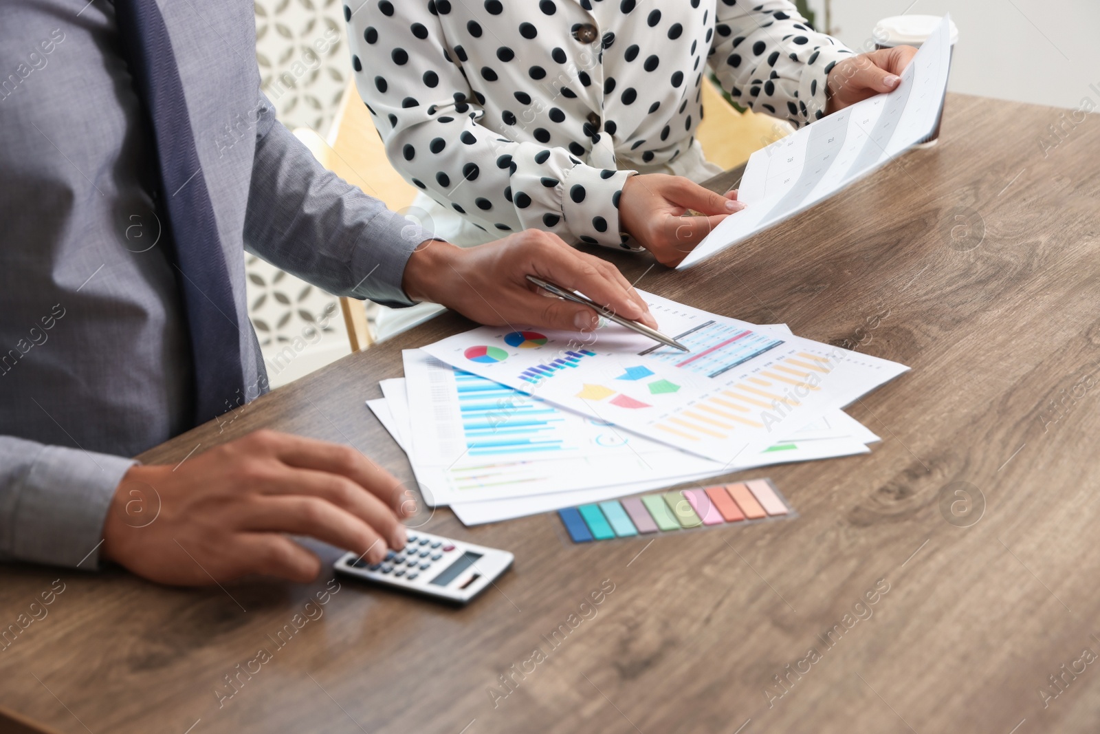 Photo of Business planning. Woman and man with calendar and documents at wooden table in office, closeup