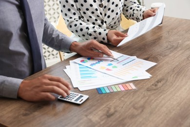 Photo of Business planning. Woman and man with calendar and documents at wooden table in office, closeup
