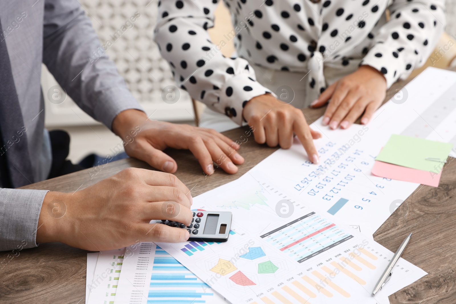 Photo of Business planning. Woman and man with calendar and documents at wooden table in office, closeup