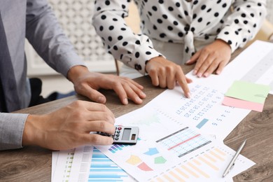 Photo of Business planning. Woman and man with calendar and documents at wooden table in office, closeup