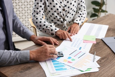 Photo of Business planning. Woman and man with calendar and documents at wooden table in office, closeup