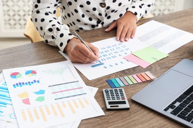 Photo of Business planning. Woman with calendar and other documents at wooden table in office, closeup