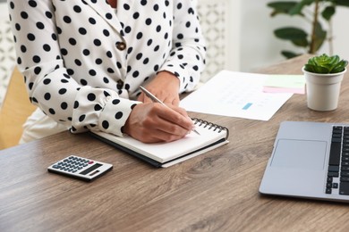 Photo of Woman using business planner at wooden table in office, closeup