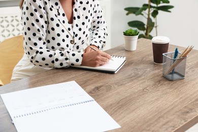Photo of Woman using business planner at wooden table in office, closeup