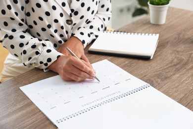 Photo of Woman using business planner at wooden table in office, closeup