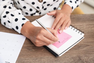 Photo of Woman using business planner at wooden table in office, closeup
