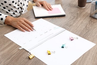 Photo of Woman using business planner at wooden table in office, closeup