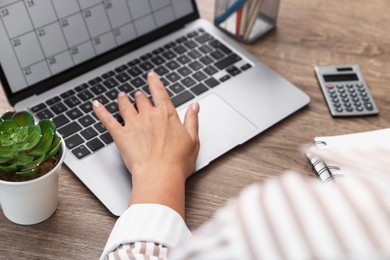 Photo of Woman using business planner and laptop at wooden table in office, closeup