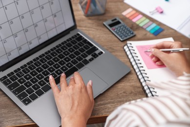 Photo of Woman using business planner and laptop at wooden table in office, closeup